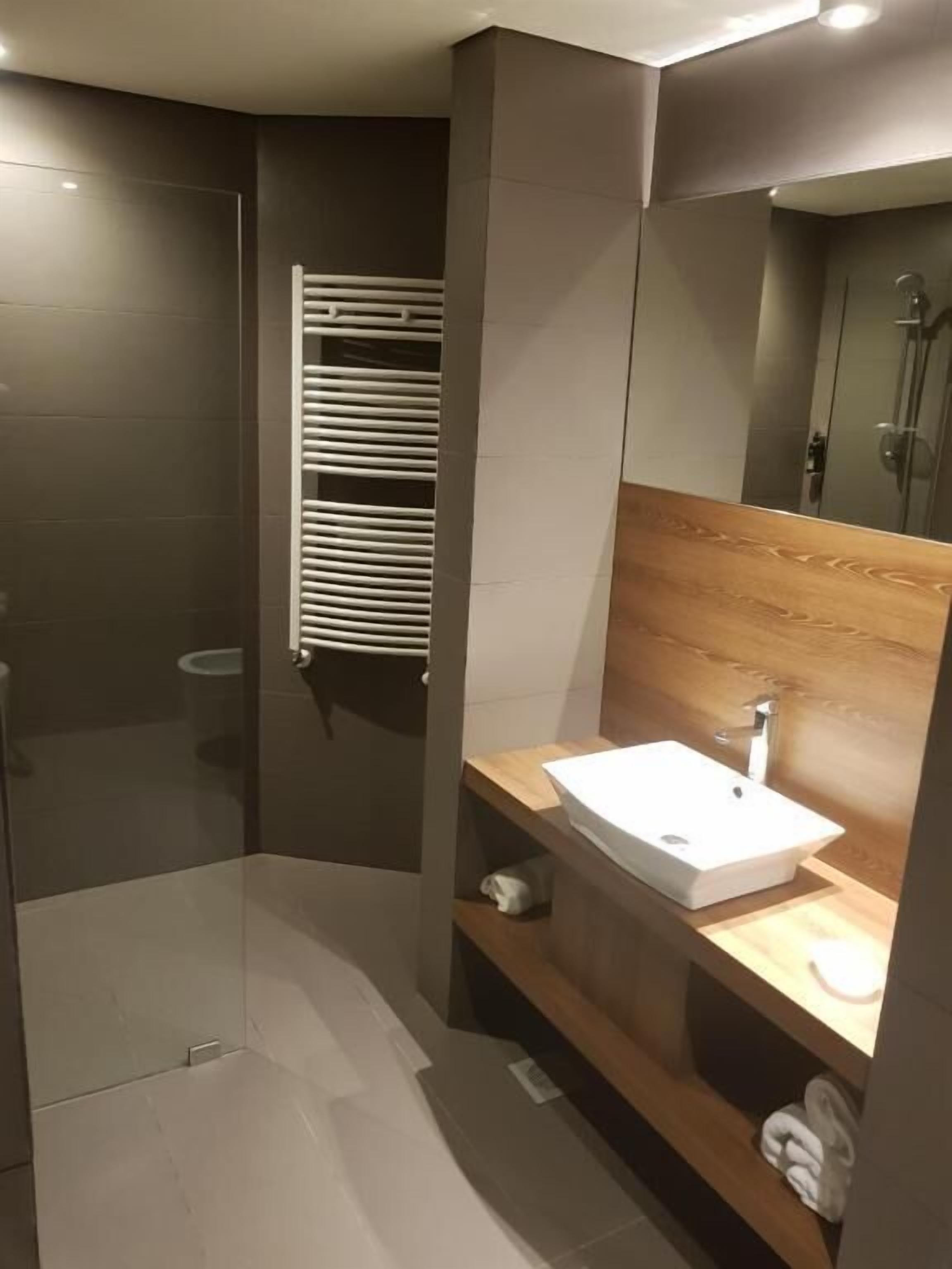 A modern bathroom with a glass shower enclosure, a white sink, and a wooden vanity.