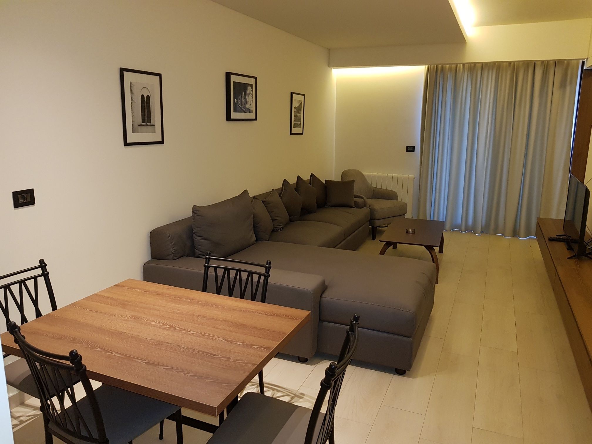 A modern living room with a wooden dining table, two sofas, and a television.