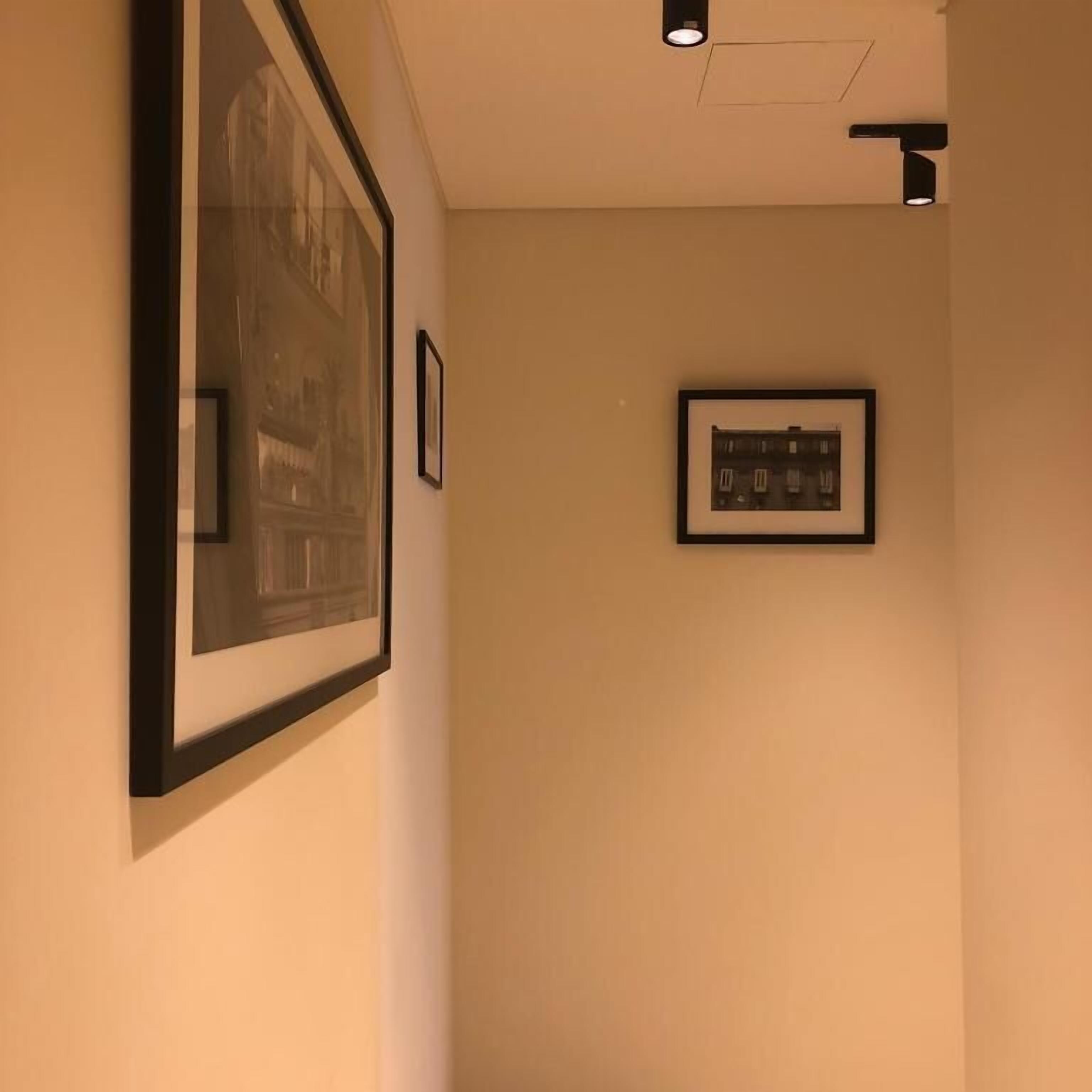 A hallway with framed pictures on the walls, a ceiling light, and a door frame.