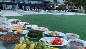 A buffet table with various fruits, vegetables, and pastries on a grassy area near a poolside. - Le Pave Residences (Ain Aar)
