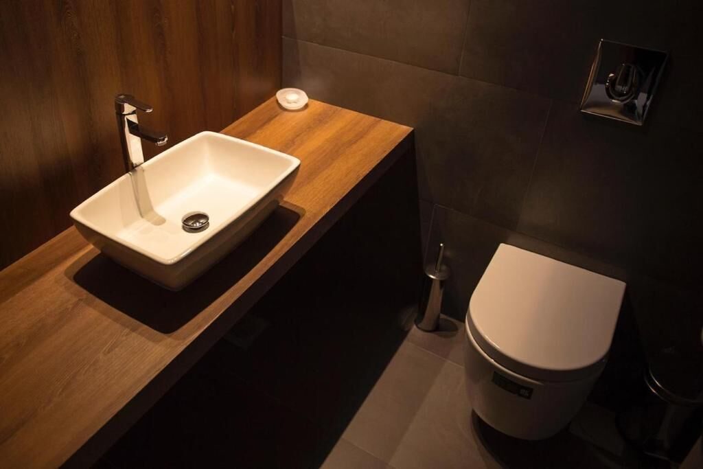 A modern bathroom with a wooden vanity, a white sink, and a toilet.