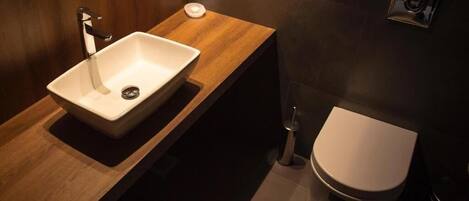 A modern bathroom with a wooden vanity, a white sink, and a toilet.