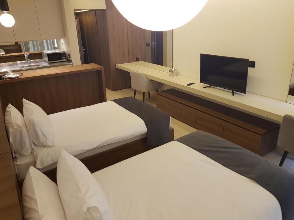 A hotel room with two beds, a desk, a television, and a kitchenette.