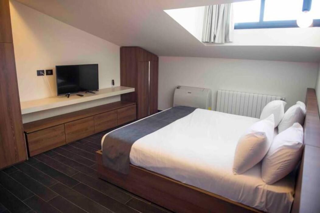 Un dormitorio con cama, televisor en un estante, ventana y radiador.