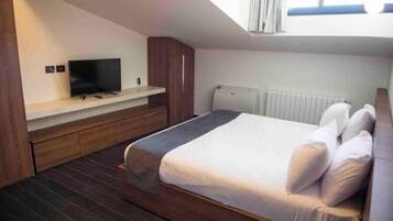 Un dormitorio con cama, televisor en un estante, ventana y radiador.