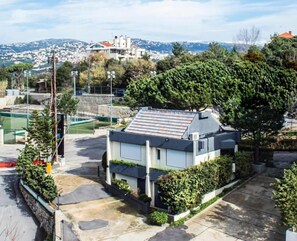 A modern house with a sloped roof, surrounded by greenery and a tennis court. - Le Pave Residences (Ain Aar)