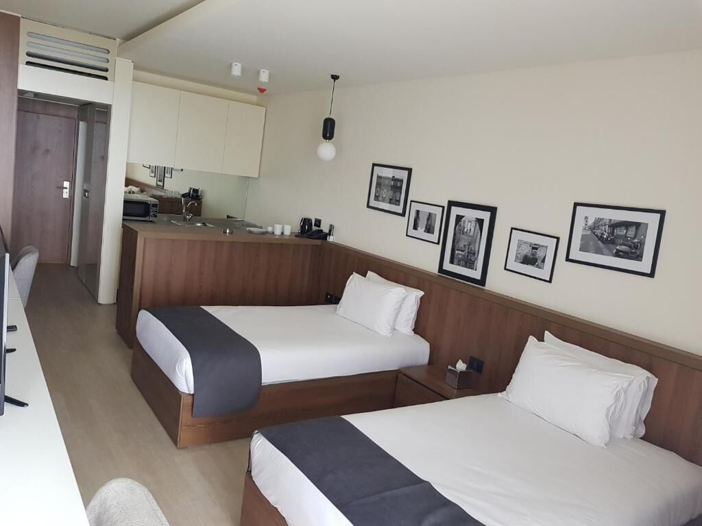 A hotel room with two beds, a kitchenette, and framed pictures on the wall.