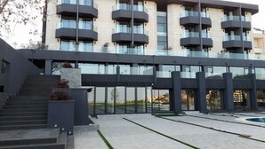 A modern building with a glass facade, multiple balconies, and a central staircase leading to the entrance. - Le Pave Residences (Ain Aar)