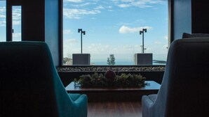 A seating area with two chairs facing a window overlooking a body of water and a bridge. - Le Pave Residences (Ain Aar)