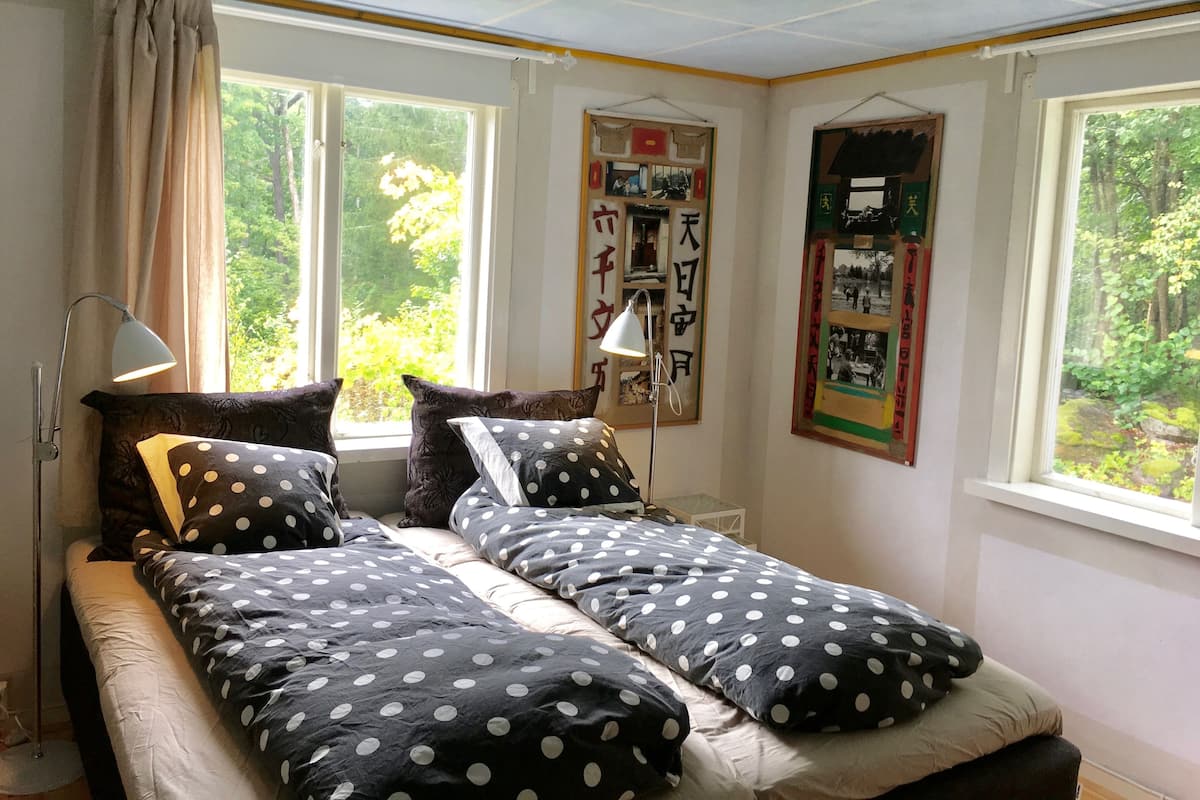 Quarto com cama, duas mesas de cabeceira, abajur e janela com cortinas.