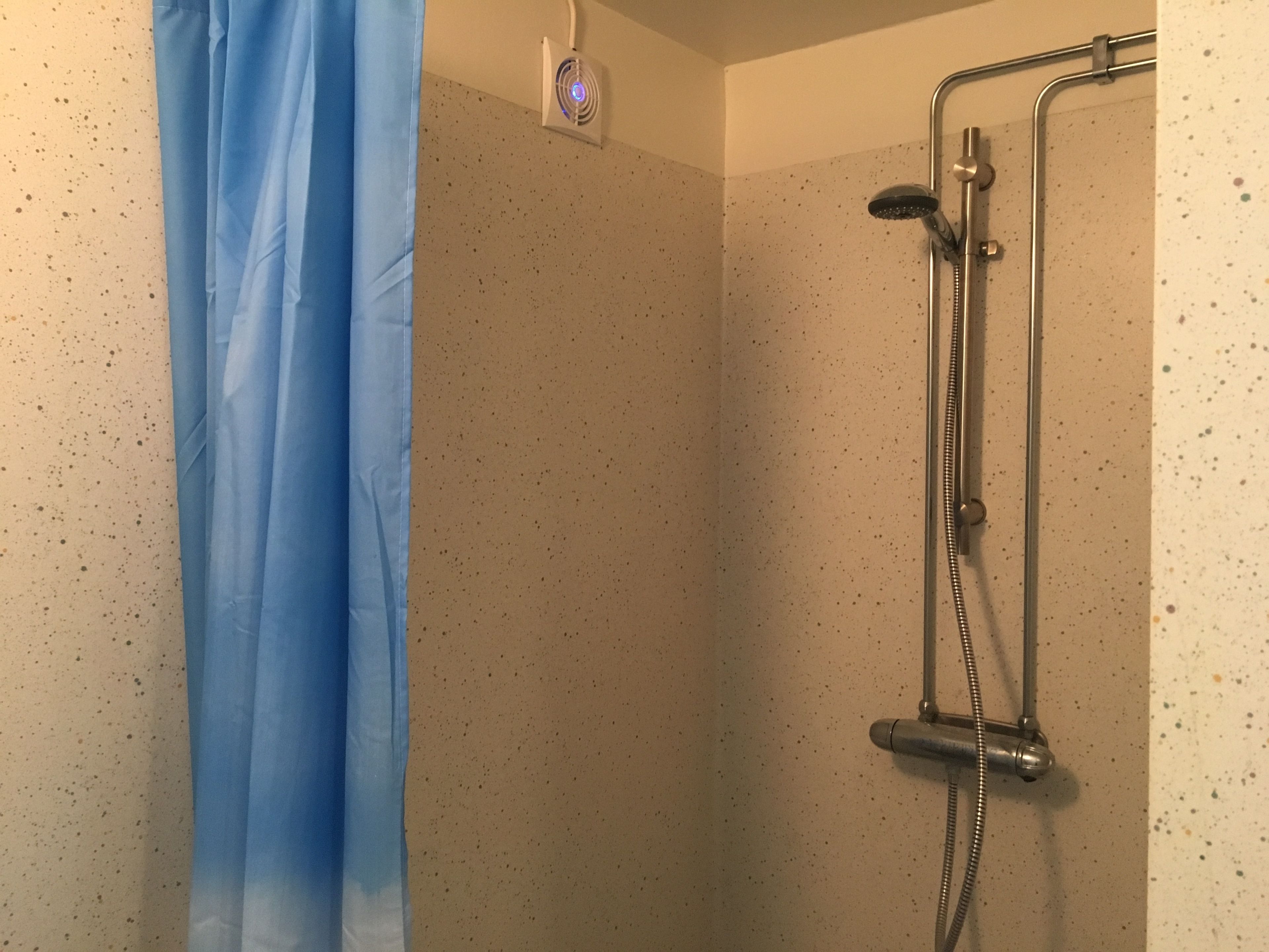 Un área de ducha con un cabezal de ducha de mano y un ventilador fijado a la pared.