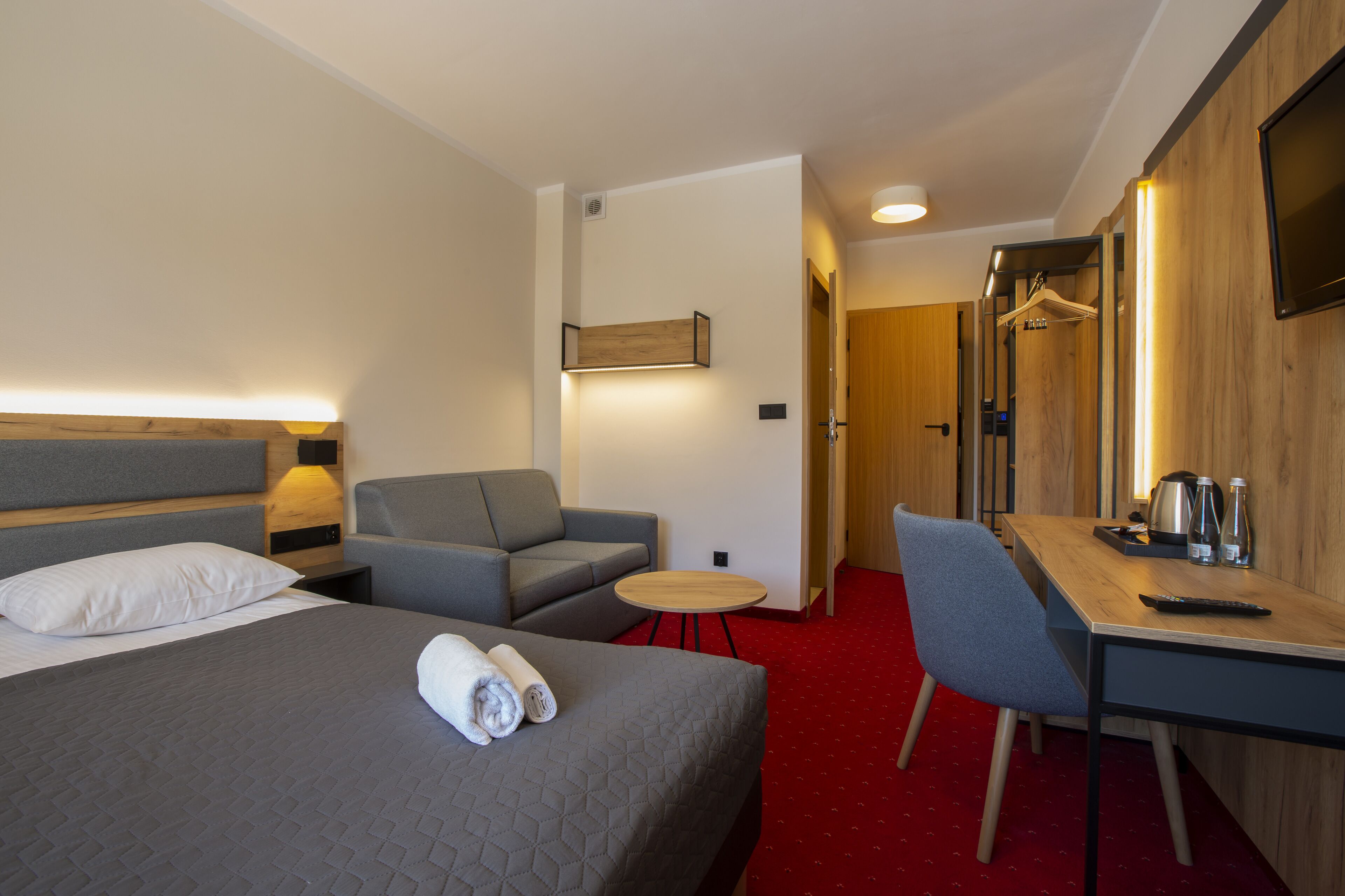 A hotel room with a bed, a sofa, a desk, and a TV.