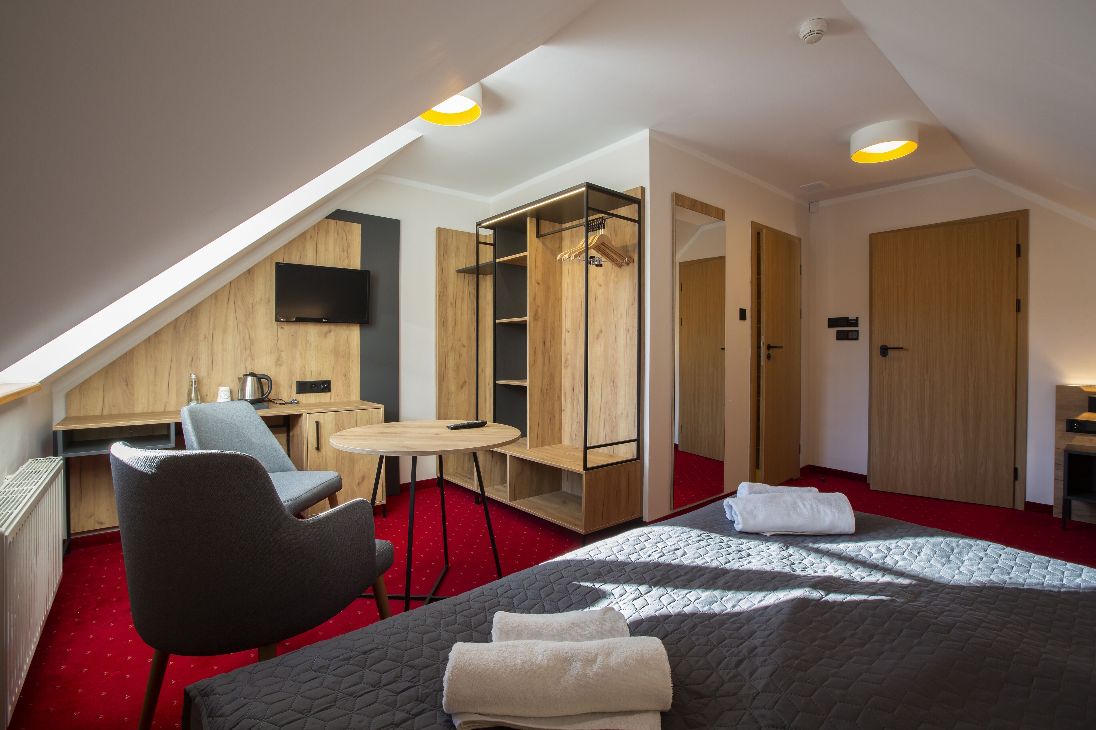 A hotel room with a bed, a desk, a chair, a wardrobe, and a small table.
