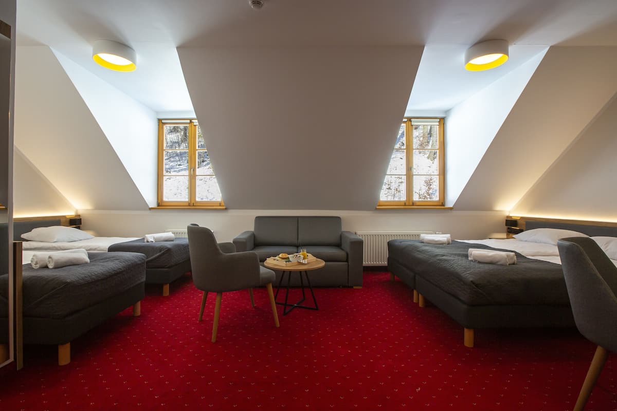 Ein Zimmer mit zwei Betten, einem Schlafsofa, einem kleinen Tisch und zwei Fenstern.