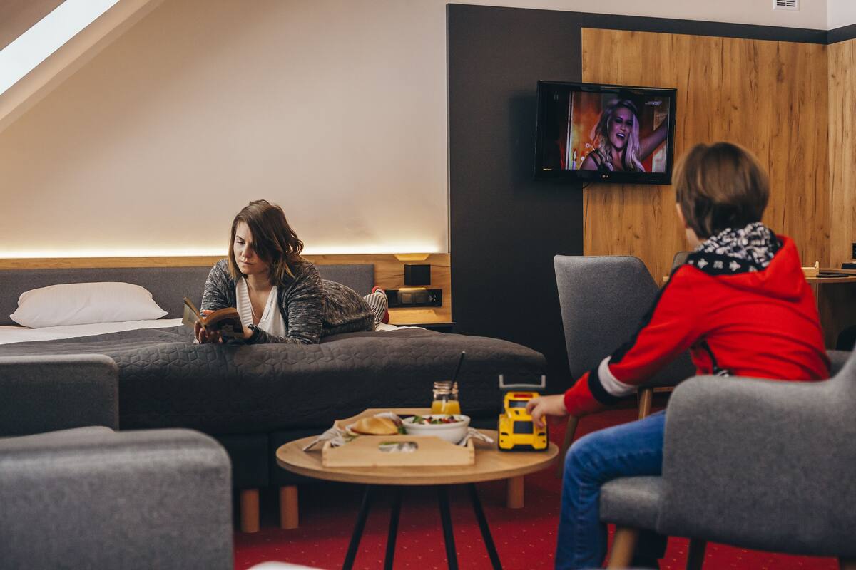 Ein modernes Hotelzimmer mit einem Bett, einem Fernseher, einem kleinen Tisch mit einem Getränk und einem Spielzeug sowie einer gemütlichen Sitzecke.