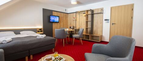 A modern hotel room with a bed, a dining table with breakfast, a TV, and a workspace.
