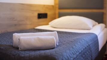 A neatly made bed with a dark quilt, two rolled towels, and a white pillow.