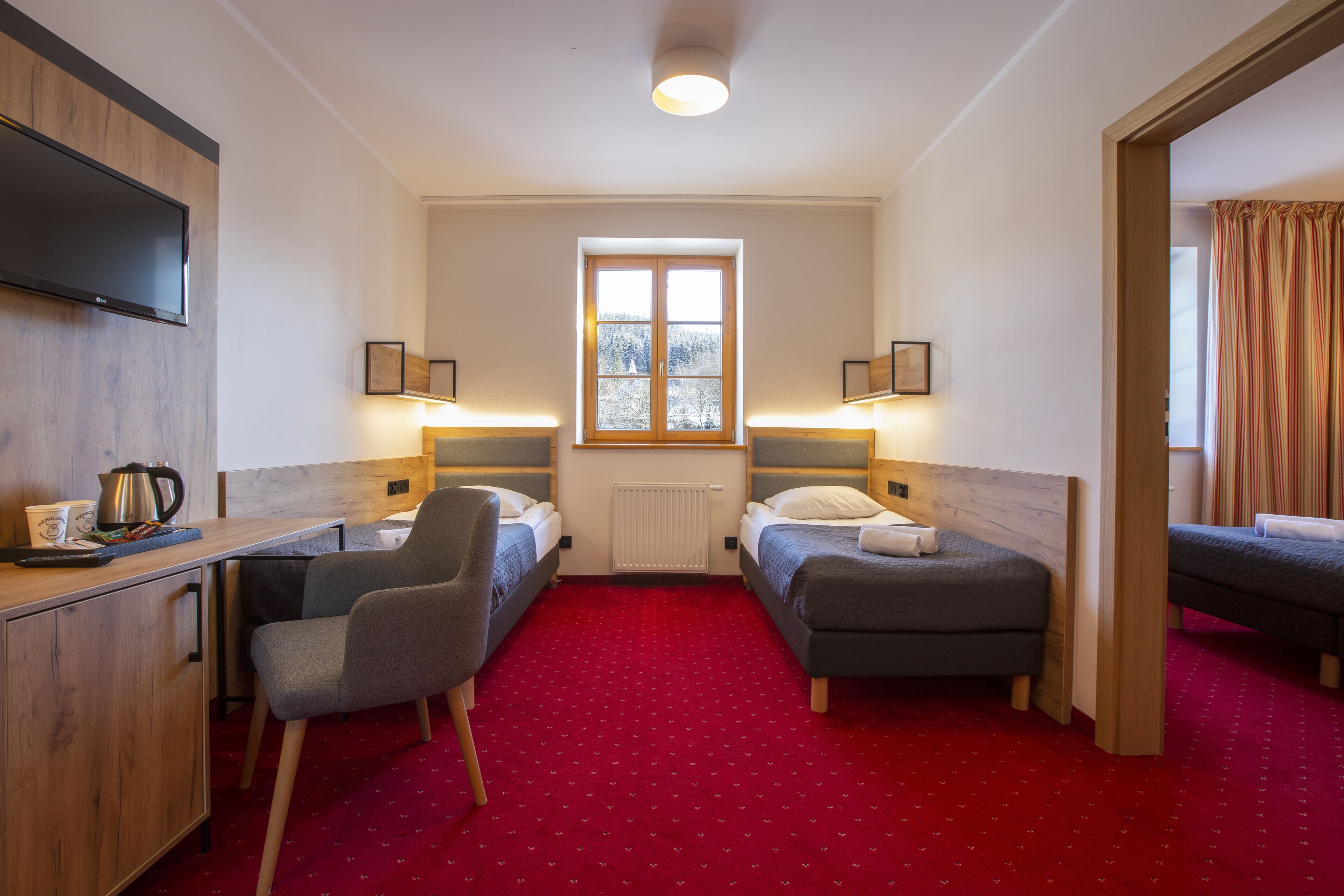 Habitación de hotel con dos camas individuales, un escritorio con silla, televisor y ventana con cortinas.