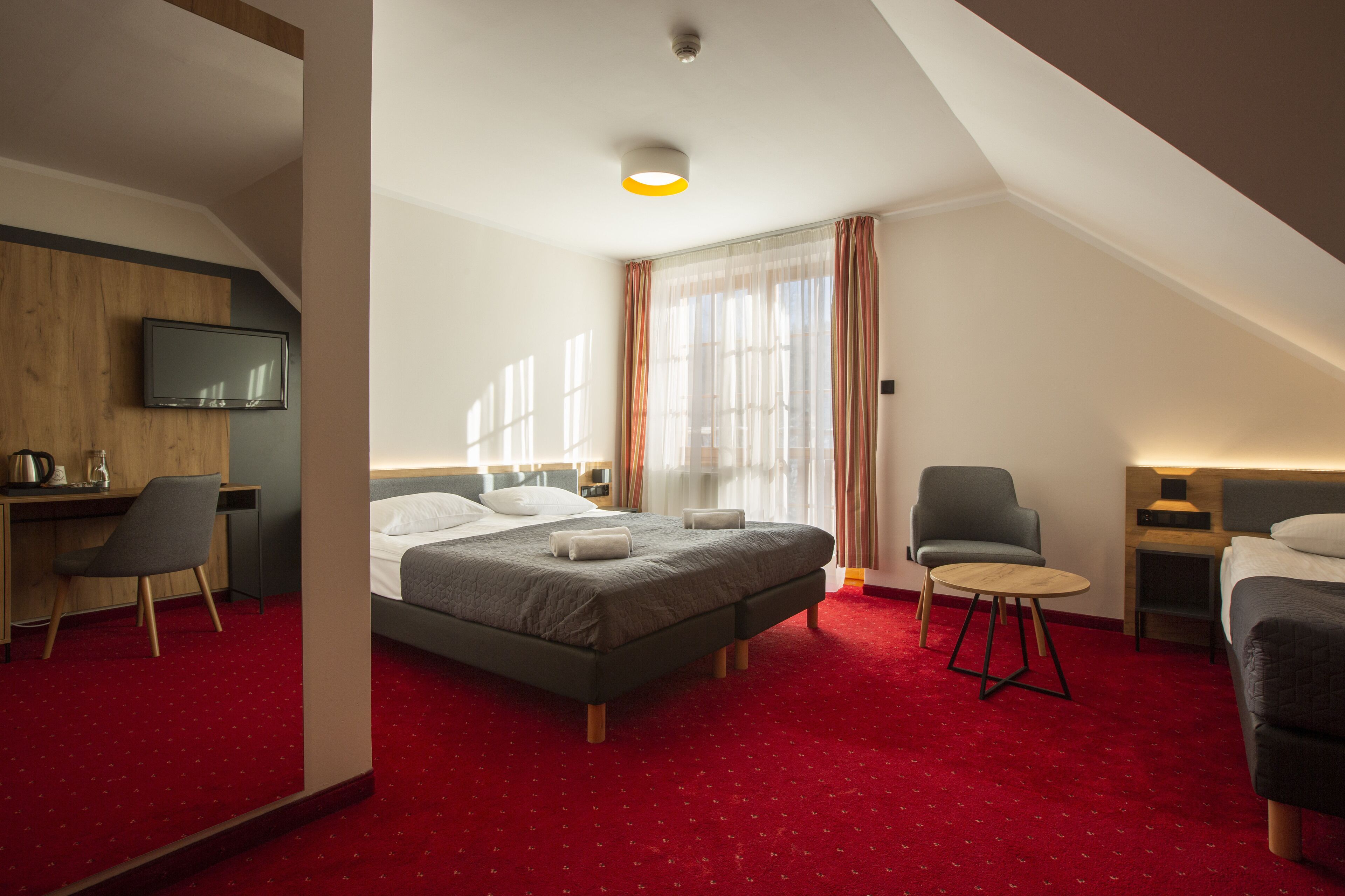 A hotel room with a bed, a desk, a chair, a TV, and a small table.