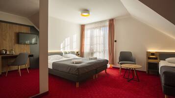 A hotel room with a bed, a desk, a chair, a TV, and a small table.