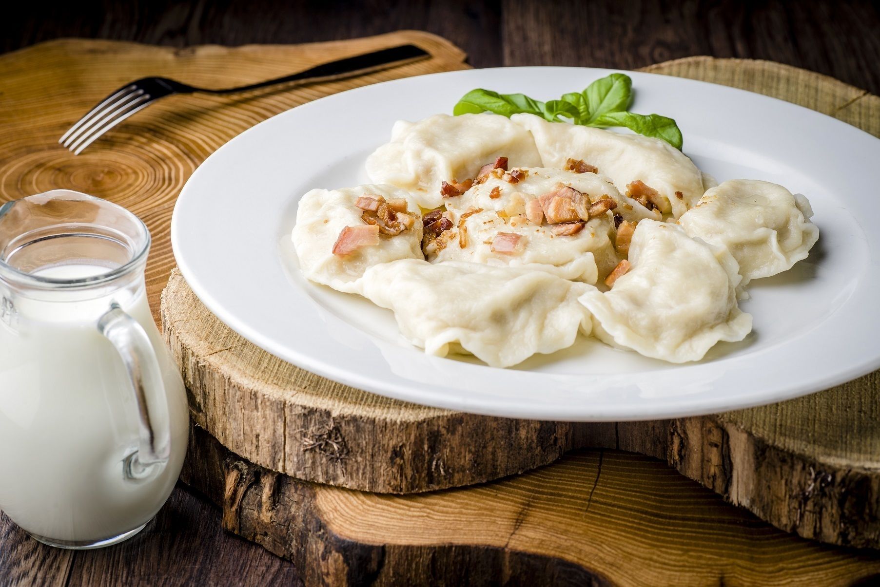 A plate of dumplings with bacon bits, accompanied by a glass of milk on a wooden table.
