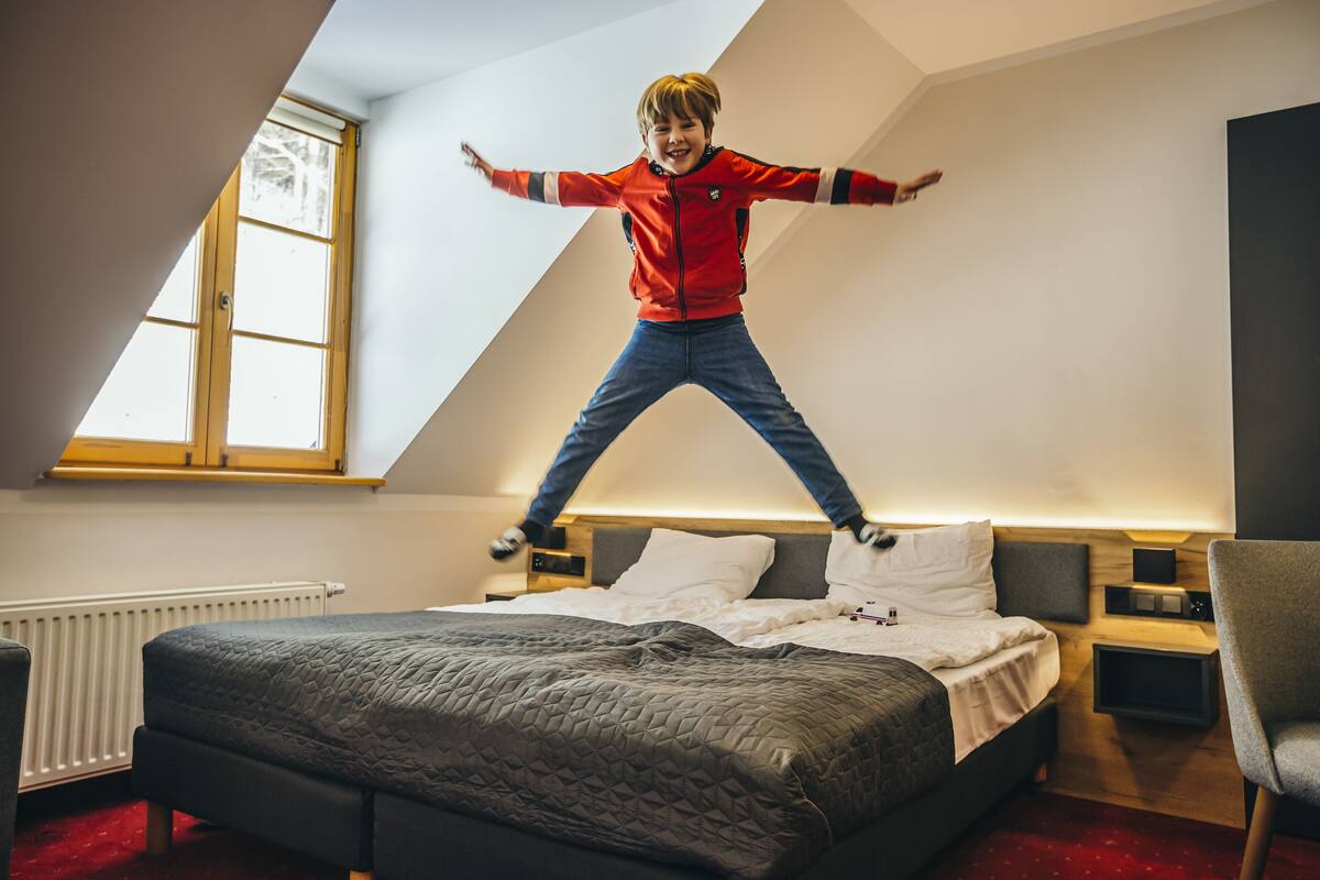 Ein Kind springt in einem Zimmer mit einem Bett, einem Fenster und einem Nachttisch.