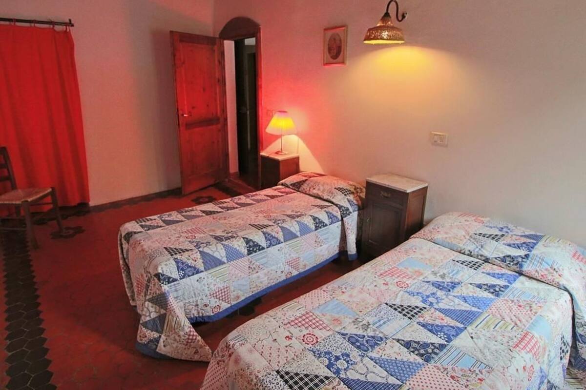 Ein Zimmer mit zwei Betten, einem roten Vorhang, einer Holztür, einer Lampe und einer Wandleuchte.