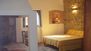 Een slaapkamer met een bed, een stoel, een tafel en een stenen muur.
