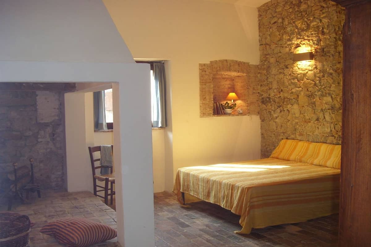 Ein Schlafzimmer mit einem Bett, einem Sessel, einem Tisch und einer Steinwand.