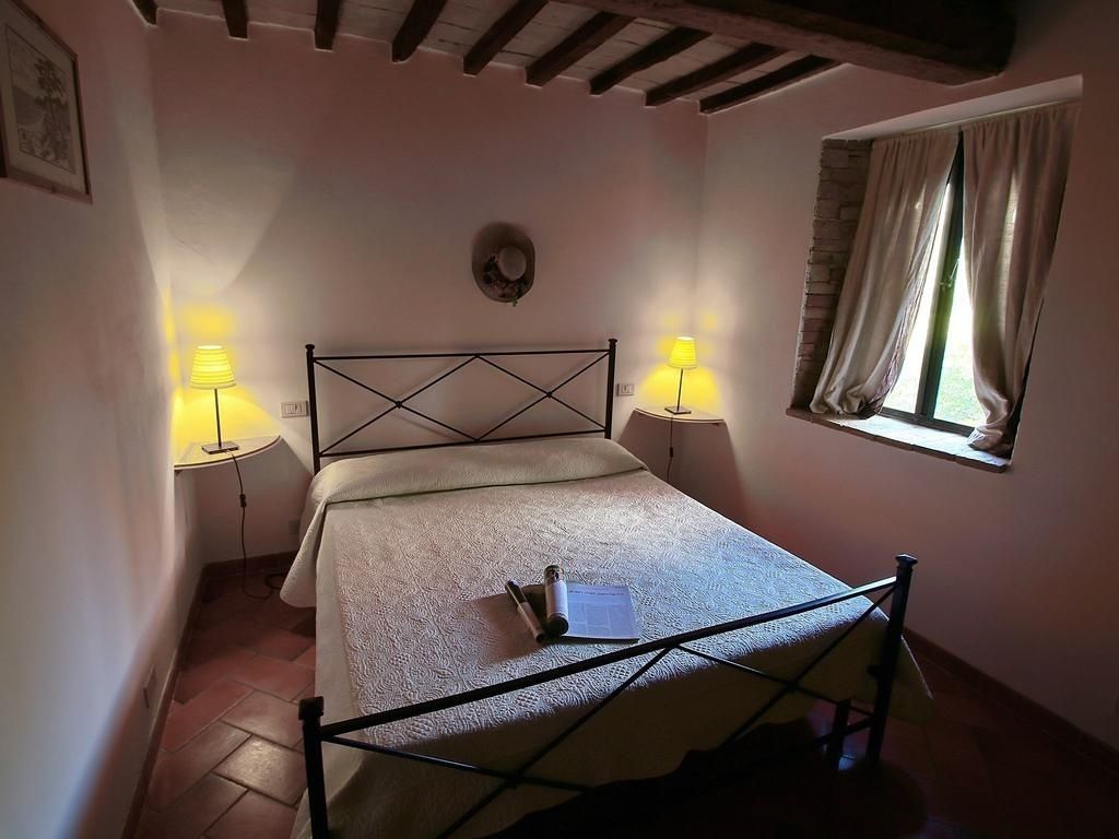 A bedroom with a single bed, two bedside lamps, a window with curtains, and a rustic ceiling.