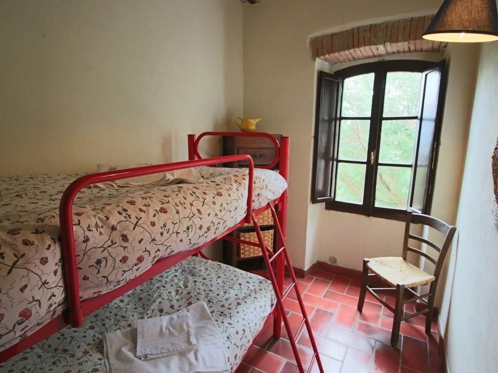 A dormitory room with bunk beds, a chair, a window, and a lamp.