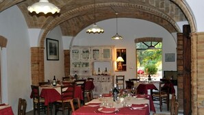 Een eetruimte met gedekte tafels, een keuken op de achtergrond en een gewelfd bakstenen plafond.