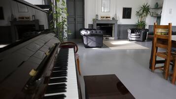 A piano in a living room with a fireplace, a dining table, and a chandelier.