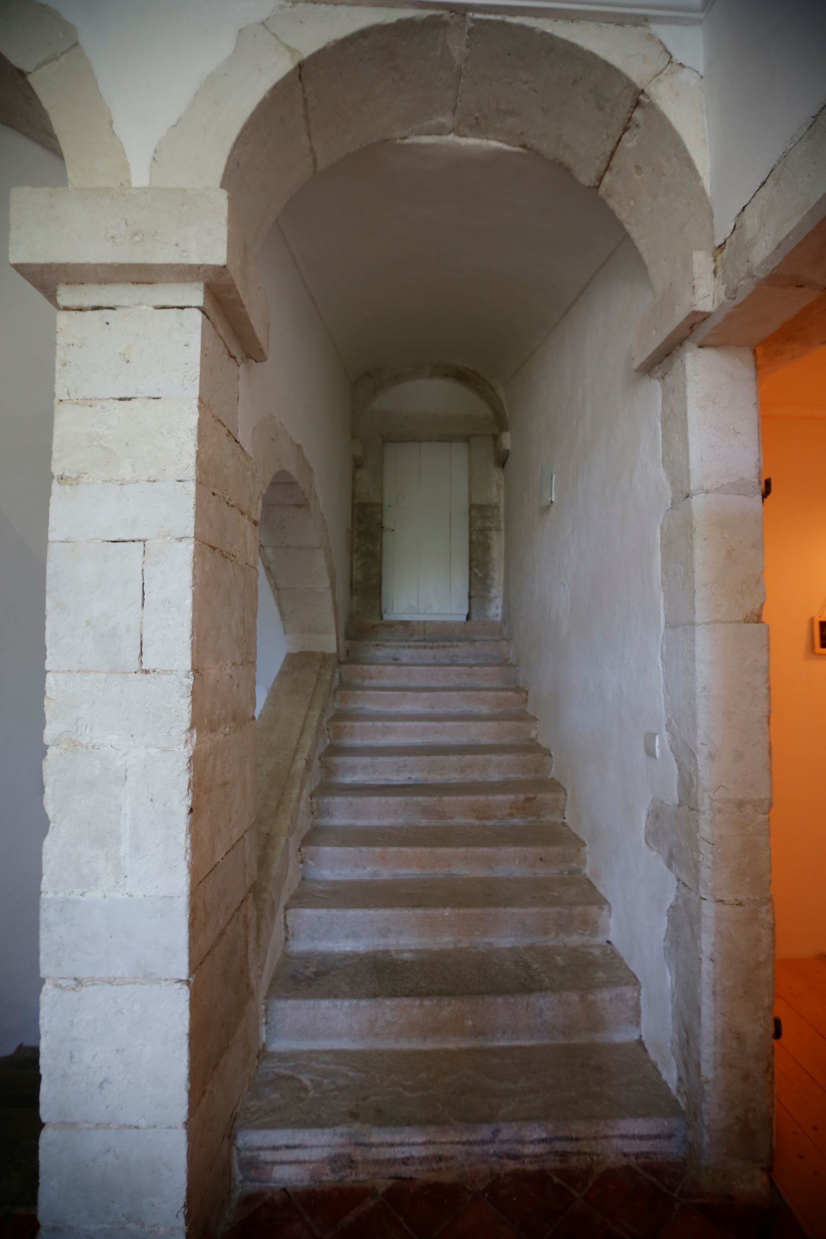 A staircase with stone steps and white walls, leading to a room with a door at the top.