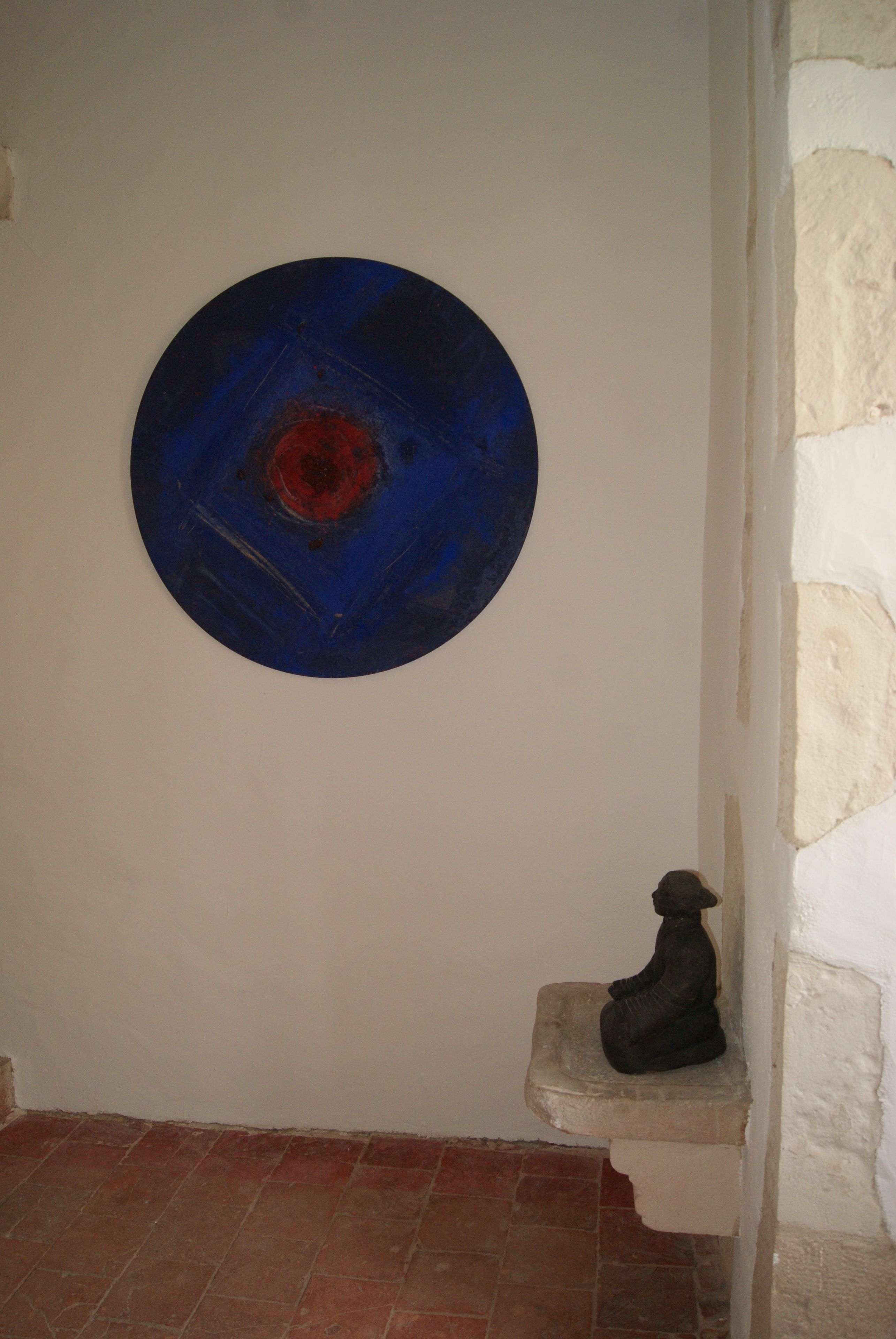 A room with a circular blue artwork on the wall, a small statue on a ledge, and a tiled floor.