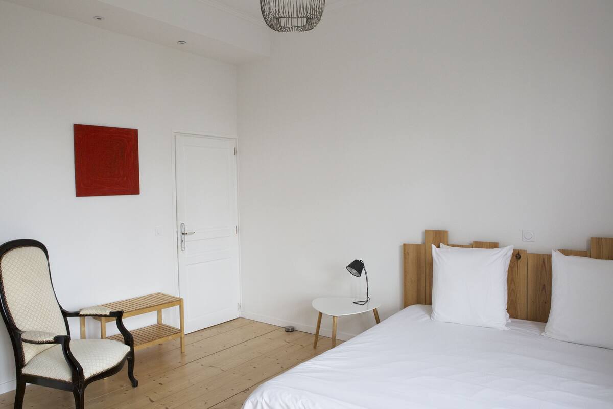 A bedroom with a bed, a chair, a small table, and a door.