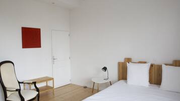 A bedroom with a bed, a chair, a small table, and a door.