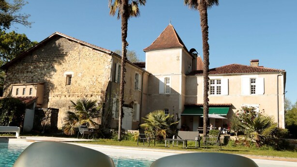 Zona junto a la piscina con dos grandes esculturas metálicas, un edificio de piedra con techo de tejas y palmeras.