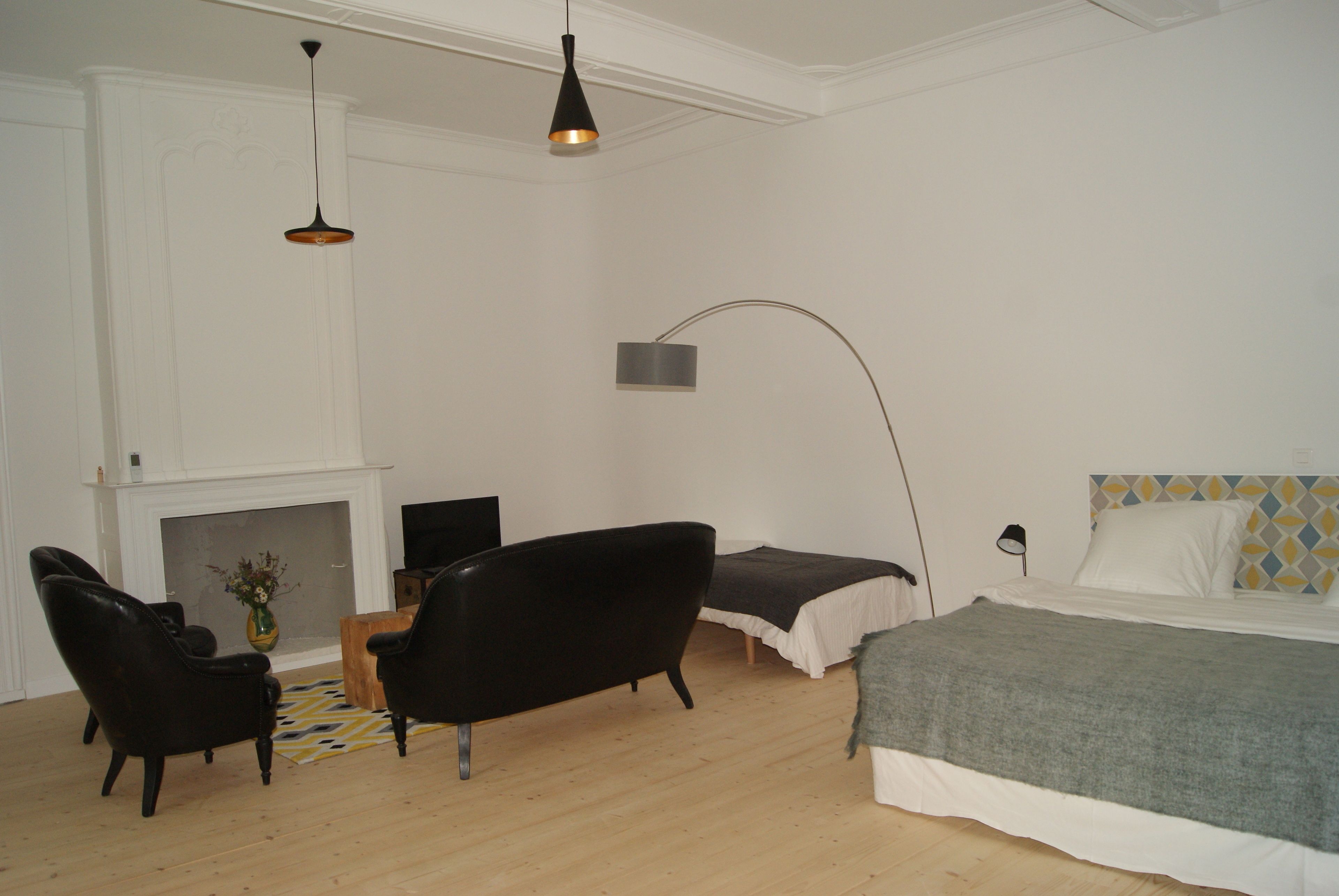A bedroom with a bed, two chairs, a fireplace, and a floor lamp.