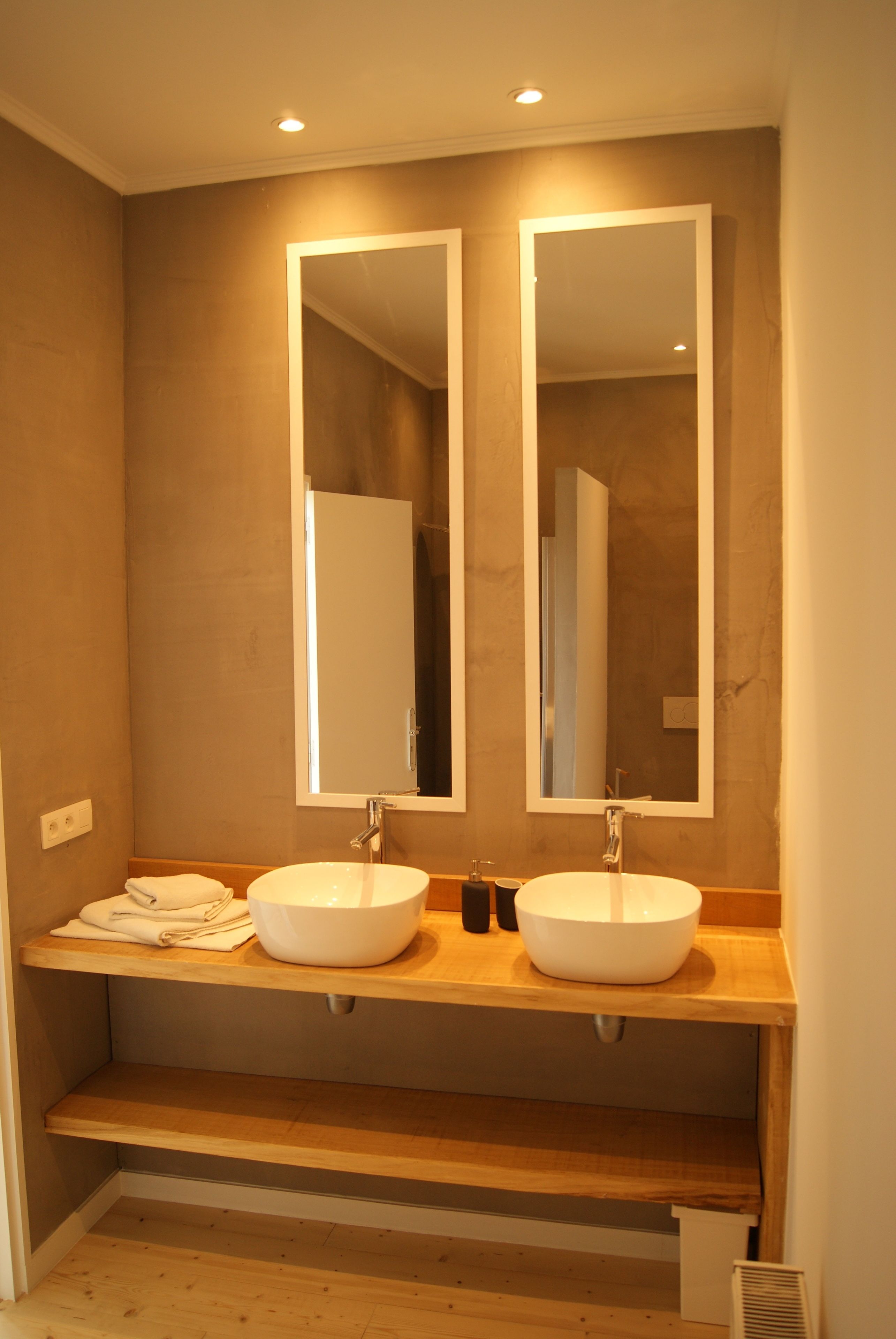 Un baño moderno con dos lavamanos, tocador de madera y espejos grandes.