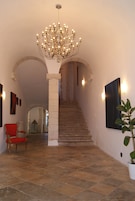 Una gran escalera con un candelabro, una silla roja y una planta en maceta.