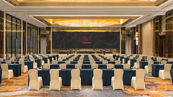 Uma sala de conferência com fileiras de mesas e cadeiras, um lustre grande e o logotipo 'Marriott' na parede.