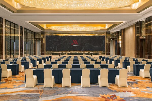 A conference room with rows of tables and chairs, a large chandelier, and a 'Marriott' logo on the wall.