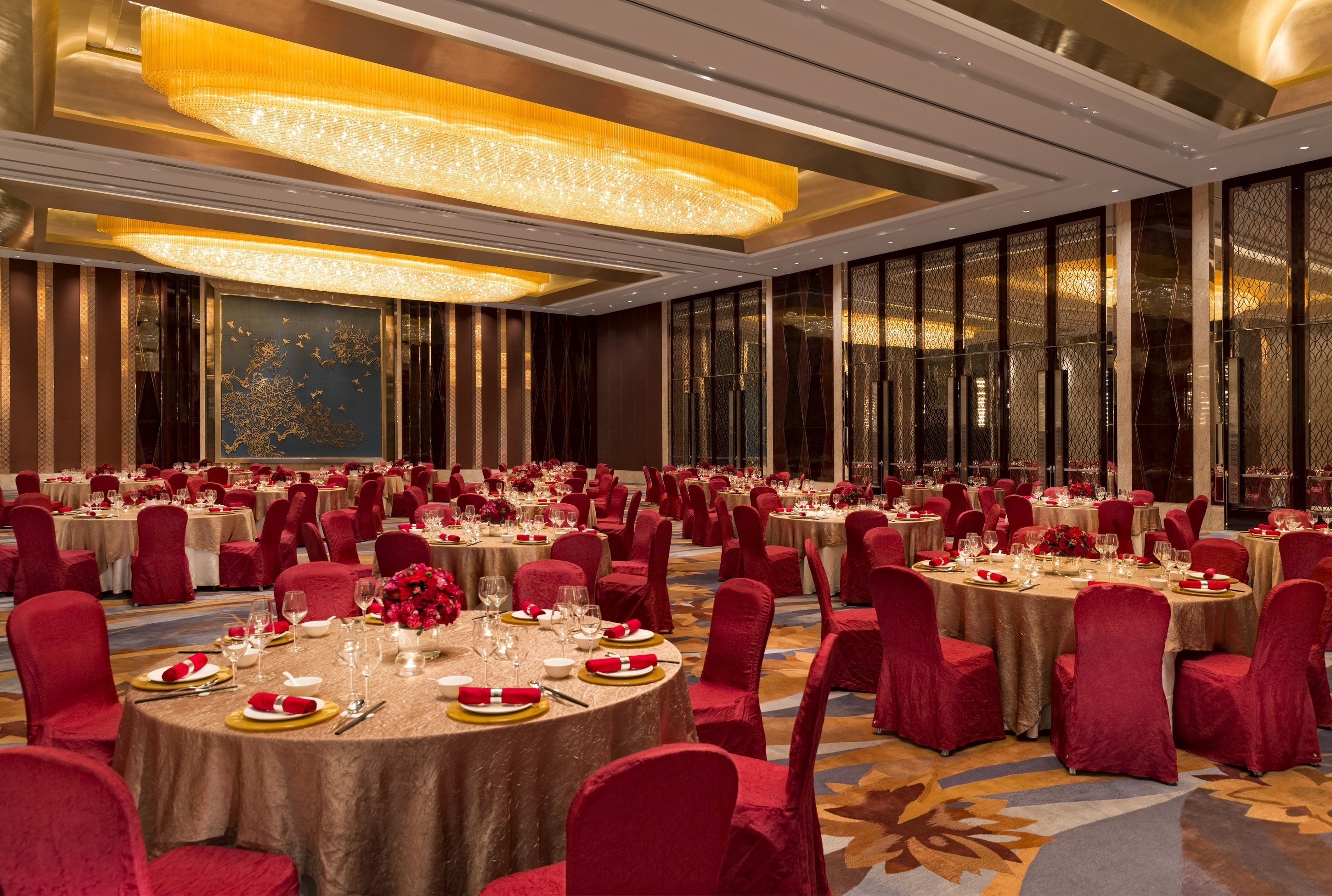 A banquet hall with round tables set for dining, red upholstered chairs, and decorative lighting fixtures.