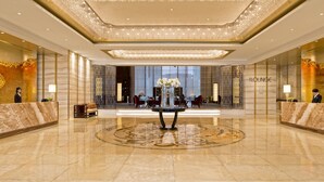 Um hall amplo com piso de mármore, uma mesa decorativa central e uma área de estar com cadeiras e mesas.