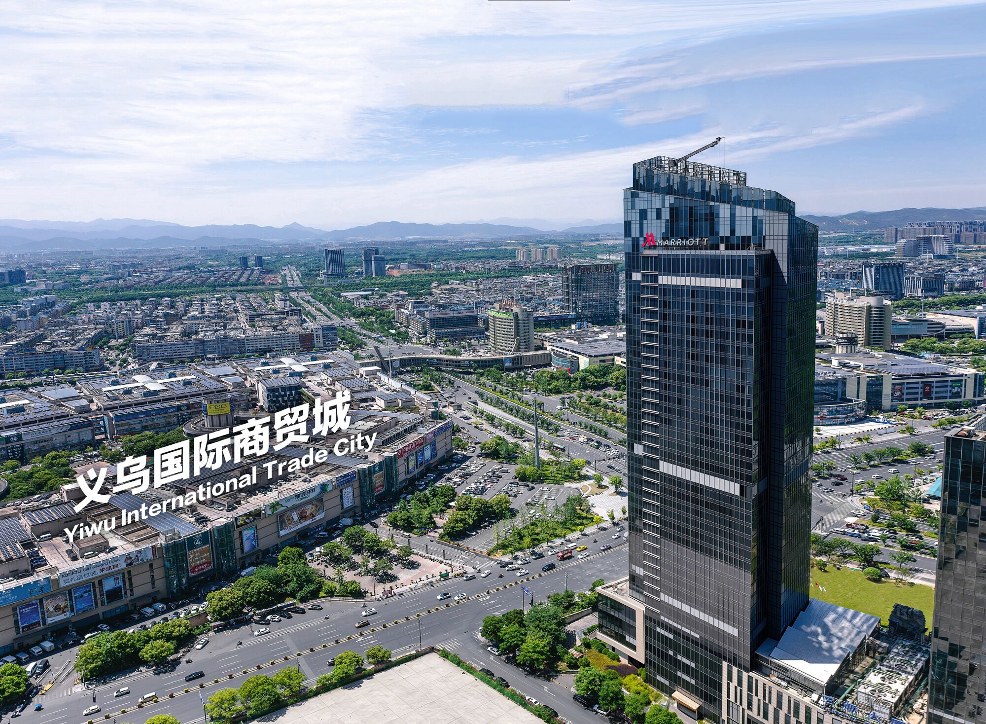 Un immeuble moderne de grande hauteur, orné du logo Marriott, entouré d’un paysage urbain avec des routes et de la végétation.