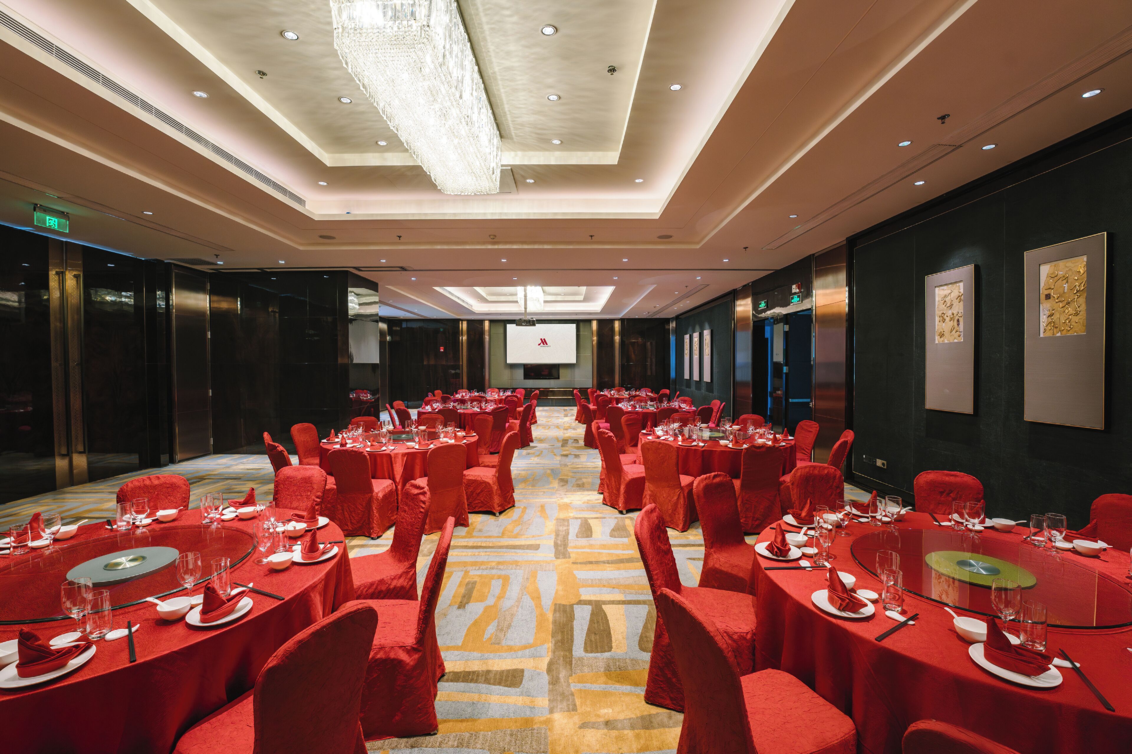 Ein Hotelkonferenzraum mit runden Tischen, roten Stühlen und Teppichboden.