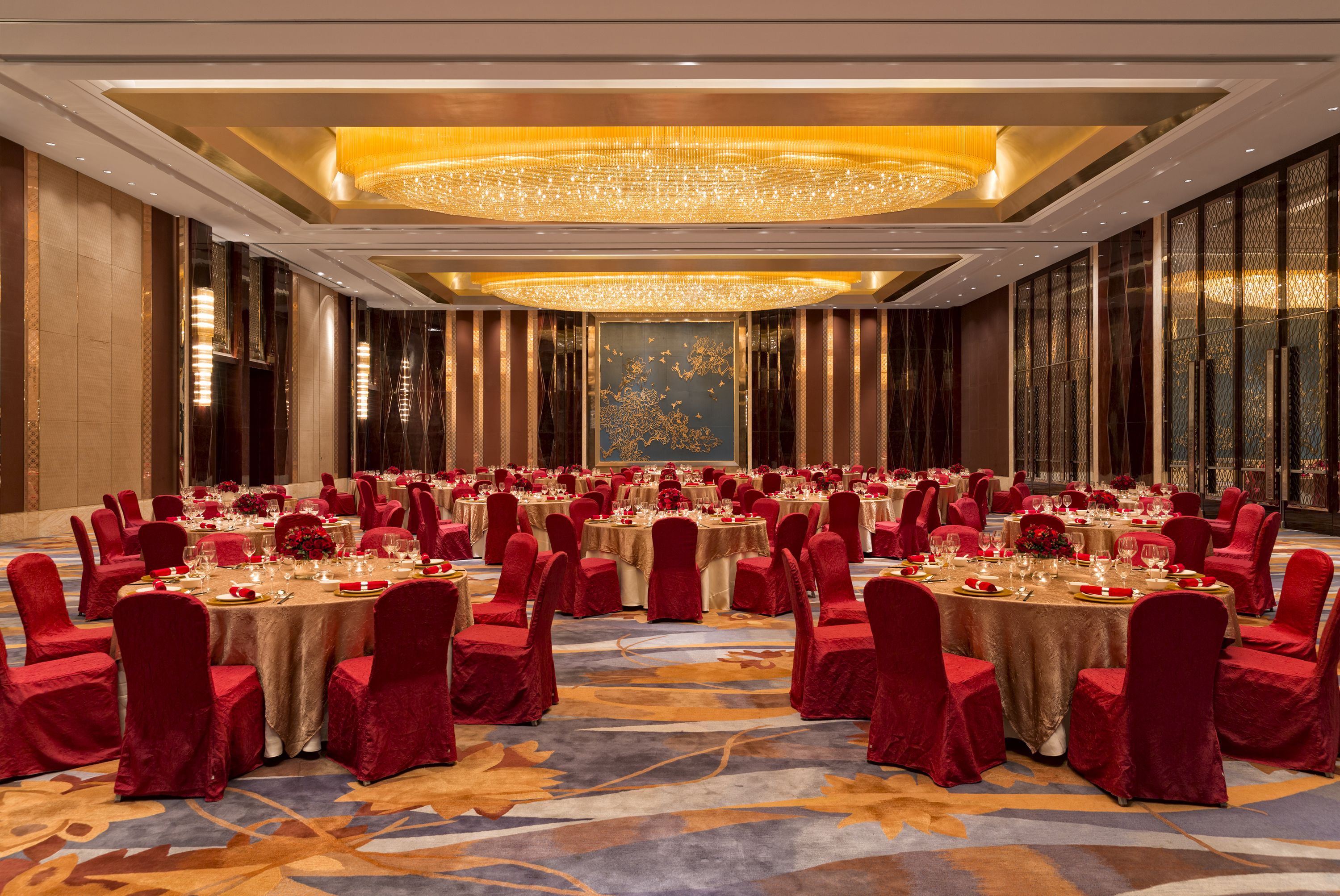 A banquet hall with round tables, red chairs, and a large chandelier.