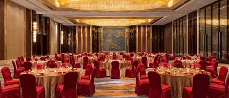 A banquet hall with round tables, red chairs, and a large chandelier.