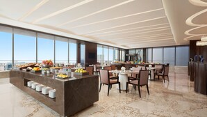 Um lobby moderno de hotel com piso de mármore, área de buffet e espaço de estar com mesas e cadeiras.
